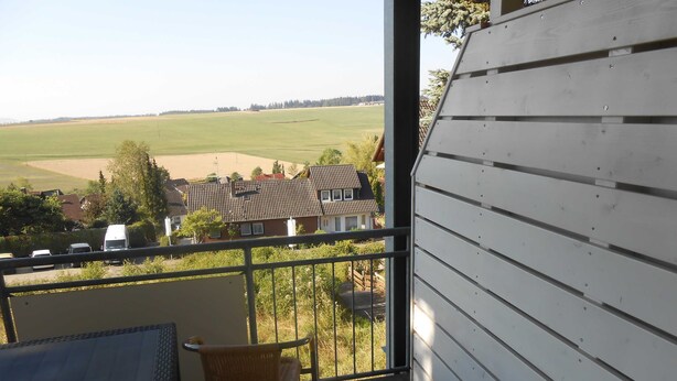 Un balcon donnant sur un champ verdoyant et des maisons.