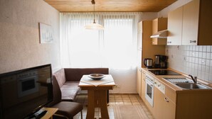Une cuisine de taille réduite comprenant un coin repas, un téléviseur et une fenêtre avec des rideaux.