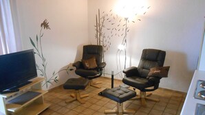 Un salon comprenant un téléviseur, deux fauteuils en cuir, une table basse en verre et un mur décoratif.