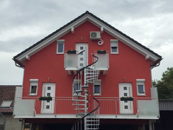 A red building with a white balcony, a spiral staircase, and a small air conditioning unit on the roof.