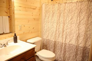 Ein Badezimmer mit Holzwänden, einem weißen Waschbecken, einer Toilette und einer Duschvorhang mit Baummuster.