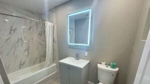Ein modernes Badezimmer mit einer Marmerdusche, einem weißen Waschbecken und einer Toilette.