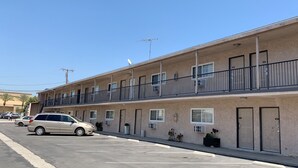 Ein zweistöckiges Motel mit separaten Zimmern, einem Parkplatz und blauem Himmel.