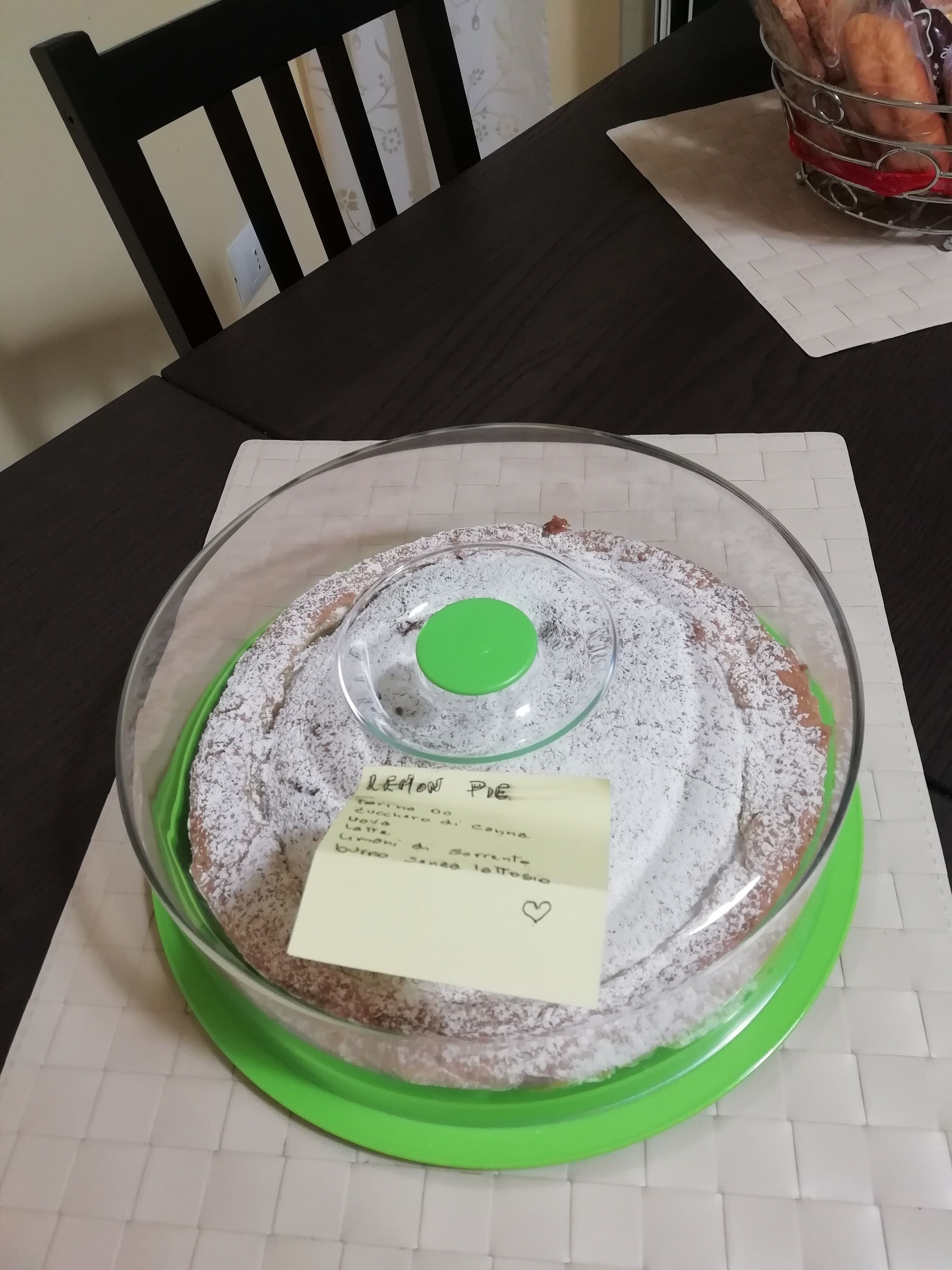 A round glass cake stand with a label on it, placed on a table with a white grid pattern.