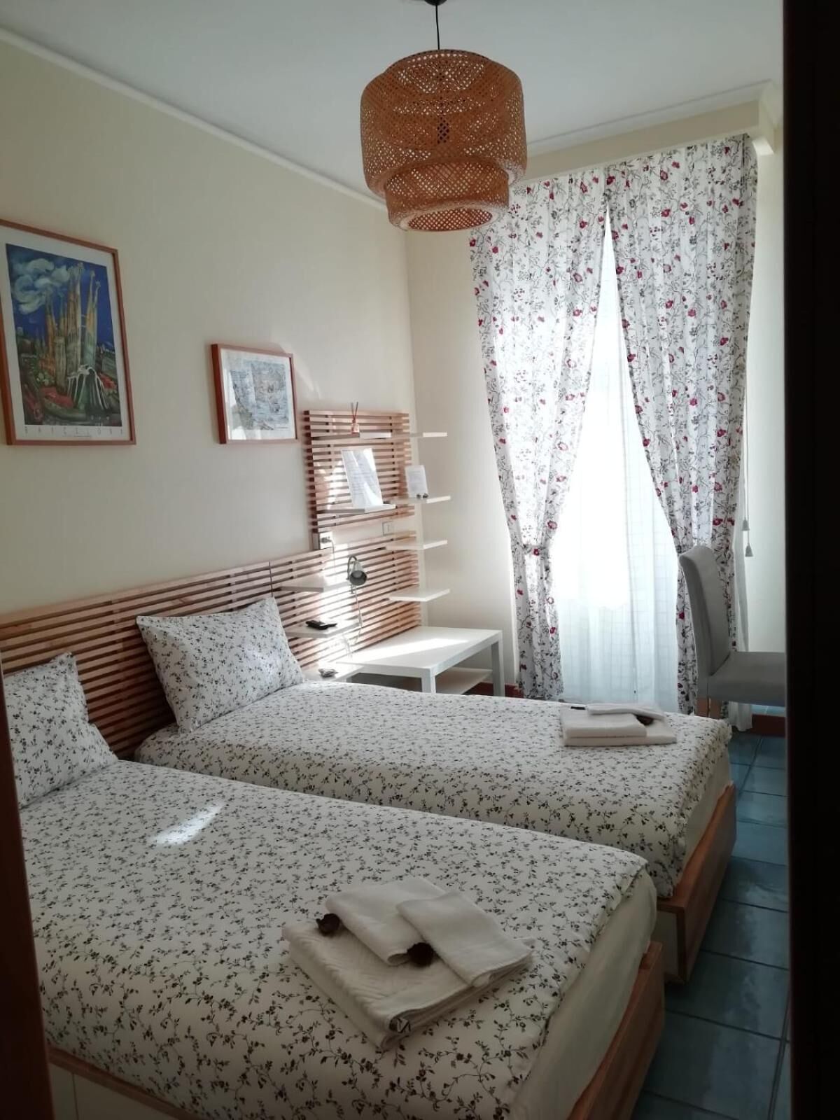 A hotel room with two beds, a wooden headboard, a small table, a lamp, and a hanging light fixture.