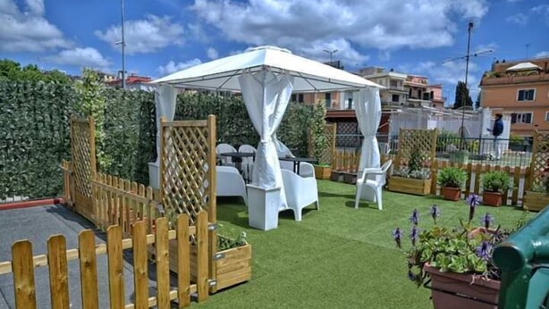 Un espacio al aire libre con patio, un toldo blanco, sillas blancas y una valla de madera.