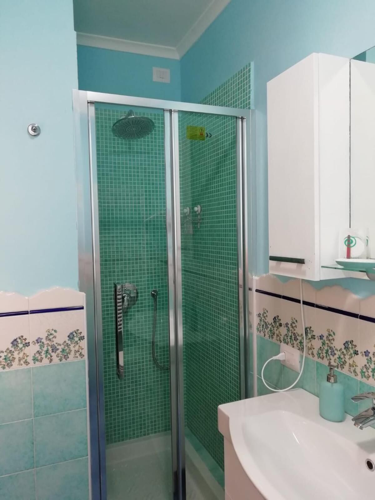 A bathroom with a glass-enclosed shower, a sink with a mirror, and tiled walls.