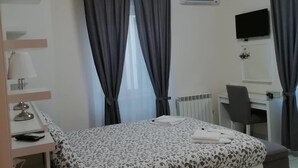 Una habitación de hotel con cama, escritorio, silla, televisión y unidad de aire acondicionado.