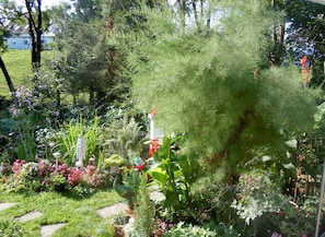A garden with various plants and flowers, a bird sculpture, and a house in the background. - Holiday island on the Dreisam - Apartment 2_ 26 sqm (Kirchzarten)