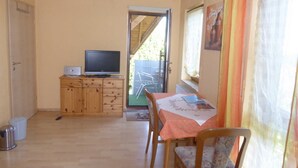 Une petite pièce comprenant un meuble en bois, un téléviseur, une table à manger avec une chaise, et une fenêtre avec des rideaux.