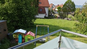 Un balcon avec une table en verre et deux chaises, donnant sur une pelouse verdoyante et un espace de jeux pour enfants.