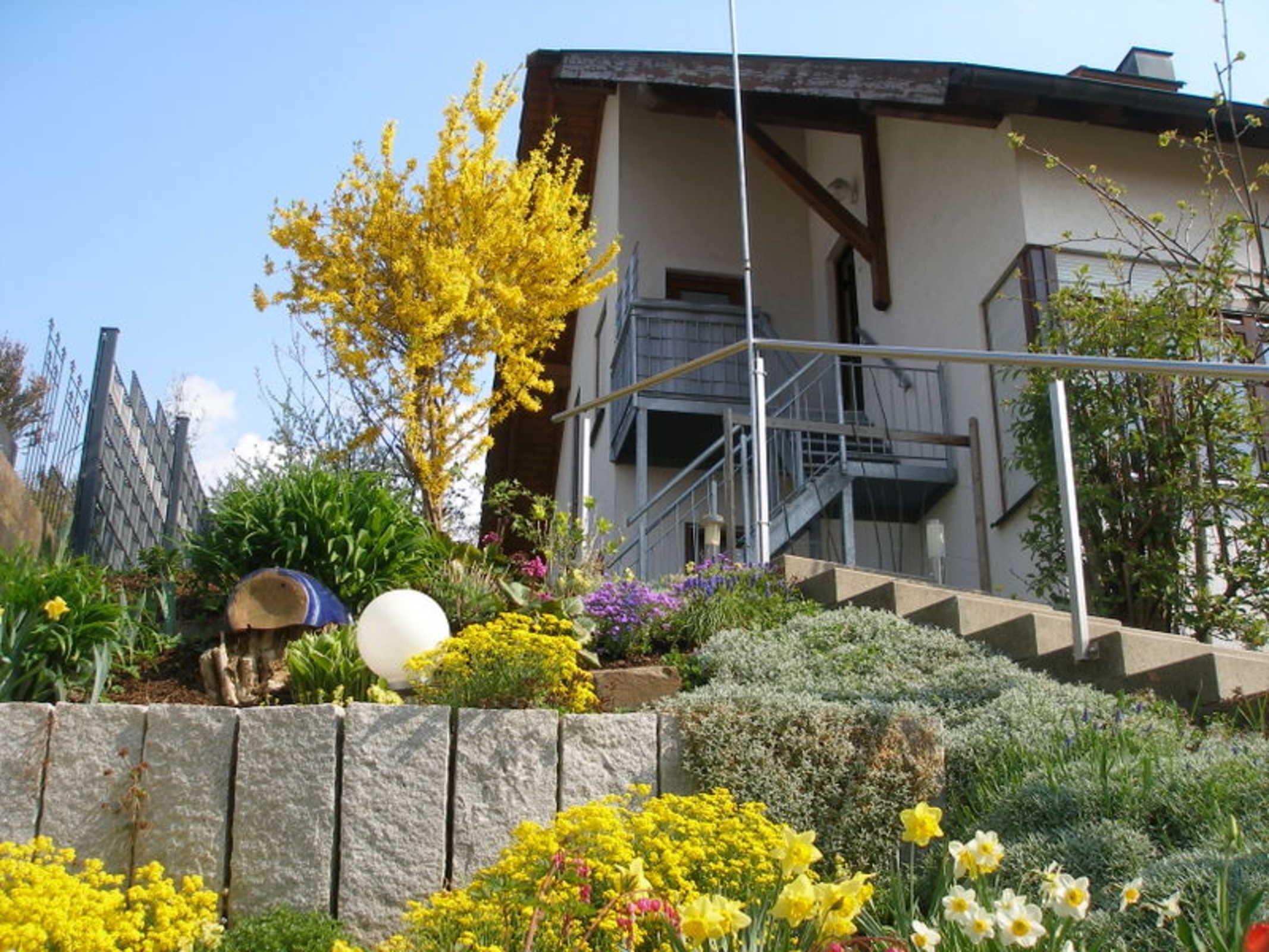 Un edificio con una escalera que conduce a un nivel superior, rodeado de diversas plantas y flores.