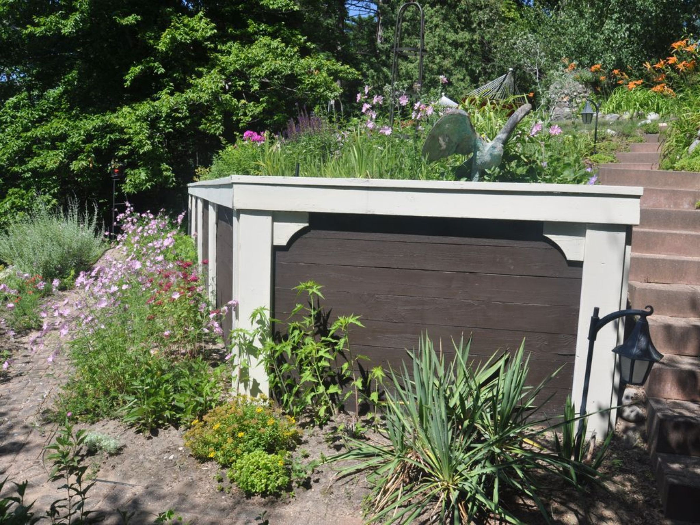 Un jardín con un portón de madera, varias plantas y una escalera de piedra.
