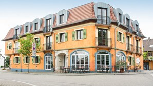 A corner building with a restaurant on the ground floor, featuring outdoor seating and a clear blue sky. - Standard - Double room - Hotel Casa Rustica (Rust)