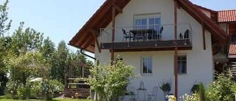 Ein zweistöckiges Haus mit Balkon, Rasen und kleinem Garten.