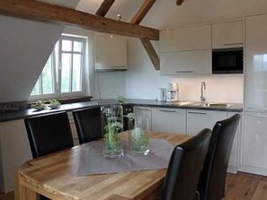 A modern kitchen with white cabinets, a wooden dining table, and a window providing natural light.