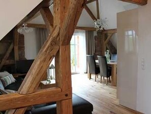 A loft-style room with exposed wooden beams, a dining area with chairs, and a view of the outdoors.