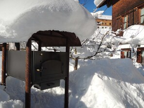 A metal outdoor utility box covered in snow, with a brick building in the background.
