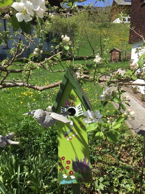 A birdhouse with a painted design, surrounded by blooming flowers and greenery. - Apartment 3 - Bir Karin - Apartment Karin (Schoppernau)