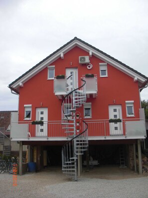 A red building with a white balcony, a spiral staircase, and a small window with a plant.