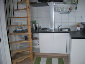 A compact kitchen with white cabinets, a wooden ladder, a sink, and a small countertop.
