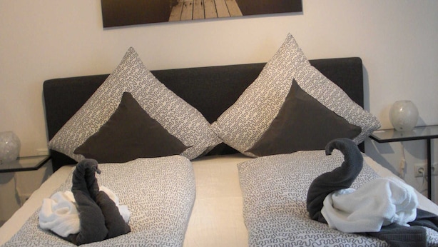 Ein Bett mit einem gemusterten Bettbezug, zwei schwanenförmige Kissen und ein Gemälde eines Piers an der Wand.