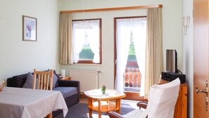 A room with a sofa, a table, a chair, a TV, and a window with curtains. - Vacation apartment 3 "Chapel" - Haus Keller vacation apartments (Todtnau)