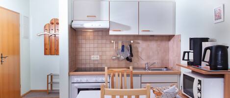 A compact kitchen with white cabinets, a stove, a microwave, and a coffee maker.