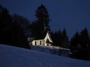 Una piccola chiesa con campanile, circondata da alberi e neve.