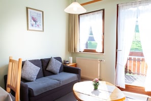 Ein Wohnzimmer mit einer Couch, einem kleinen Tisch mit einer Vase, einer Lampe und einem Fenster mit Vorhängen.