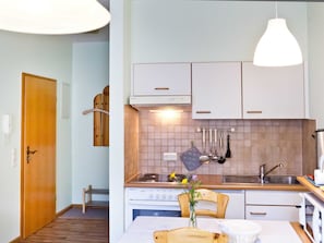 A compact kitchen with white cabinets, a wooden door, a hanging pot rack, and a dining area with a table and chairs.