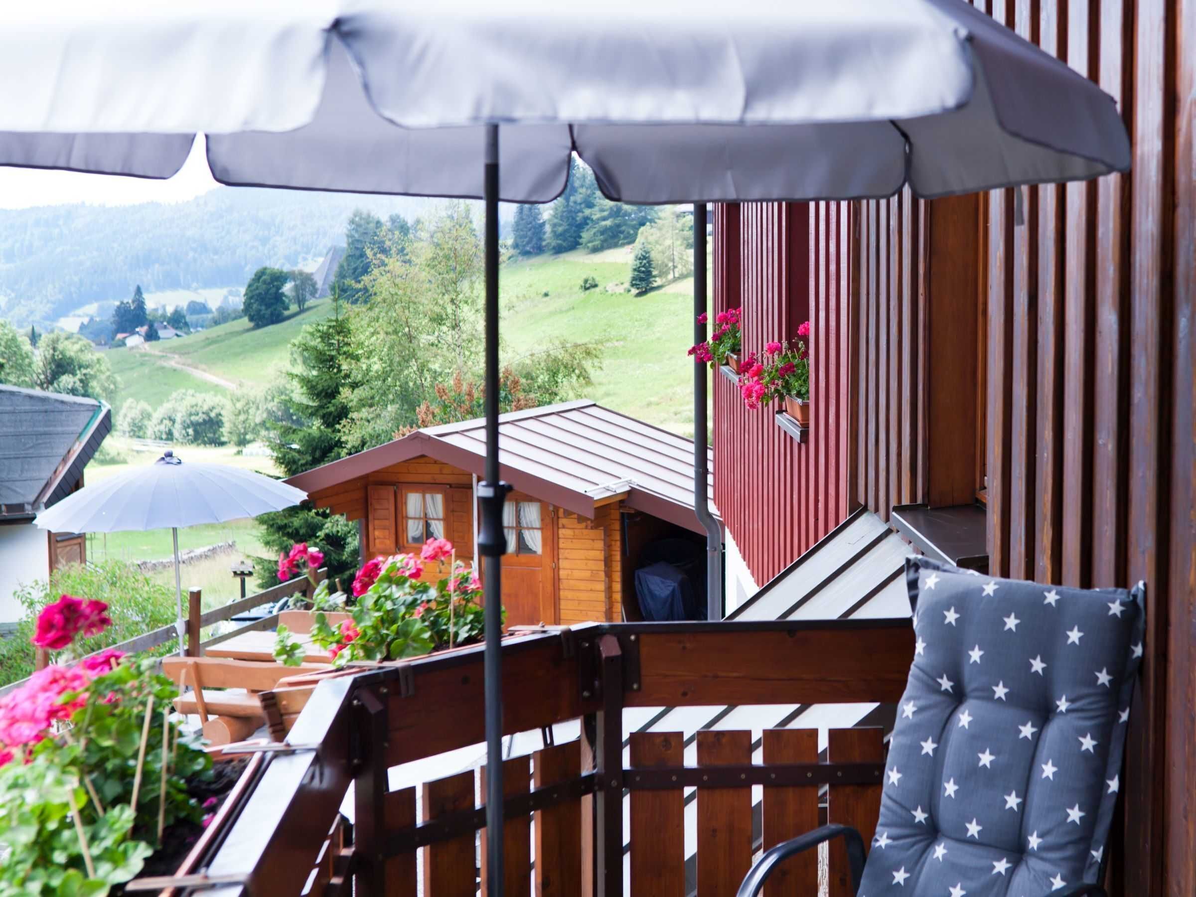 A wooden deck with a chair and an umbrella, overlooking a rural landscape with houses and greenery.