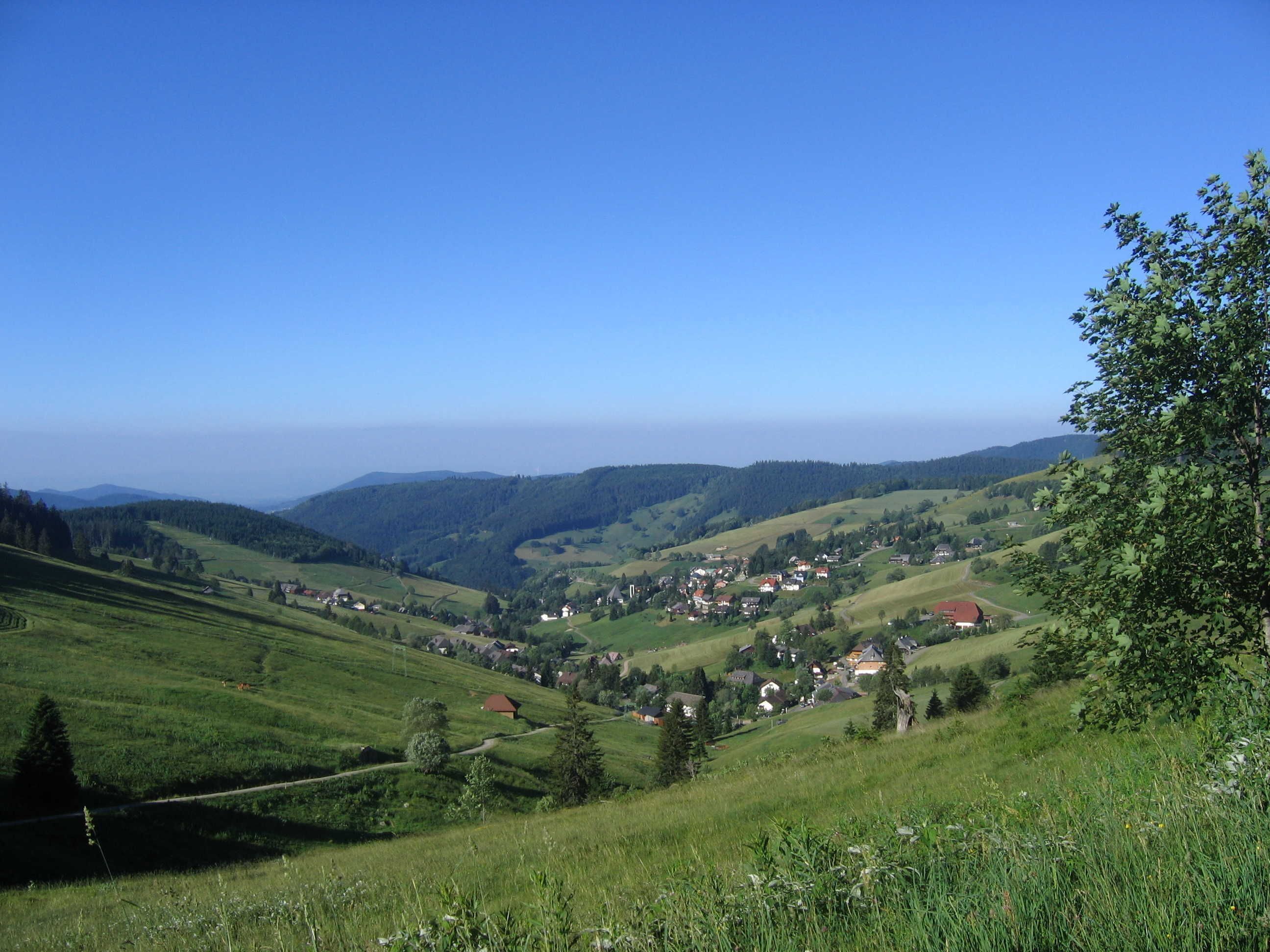 A rural landscape with rolling hills, a small village, and a clear blue sky.