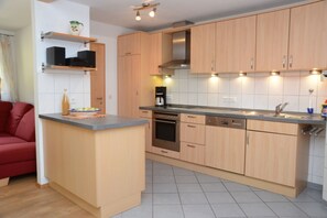 Una cocina compacta con armarios de madera, horno empotrado, lavavajillas y cafetera.