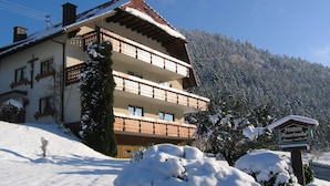 Un edificio de varios pisos con balcones, un letrero que dice 'Pension' y un entorno cubierto de nieve.