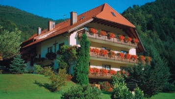 Eine zweistöckige Chalet mit Balkonen, umgeben von Grün und einer Bergkulisse.