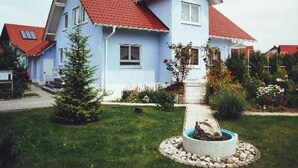 A two-story house with a red-tiled roof, a small front yard with a garden, and a circular stone feature in the center.