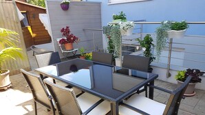 A patio with a glass-top table and wicker chairs, surrounded by potted plants and a metal trellis.