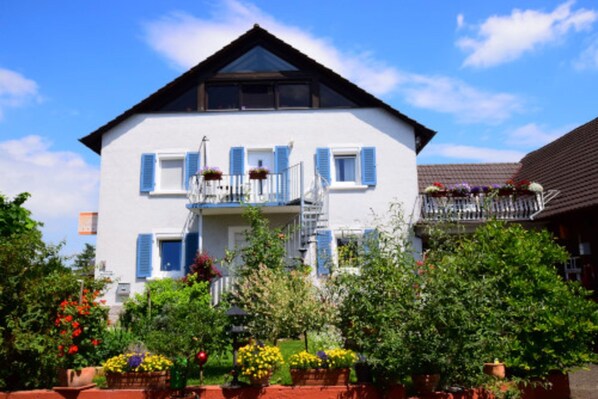 Une maison à deux étages avec un balcon, entourée de plantes et de fleurs en pot.