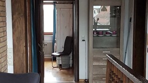 Una habitación con piso de madera, una silla negra, un radiador y una puerta que da a otra habitación.