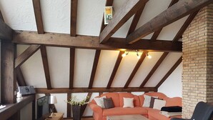 Un salón estilo loft con vigas de madera a la vista, pared de ladrillo, un conjunto de sofás, una mesa de centro y un televisor.