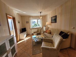 A living room with a sofa, armchair, coffee table, TV, and a window with curtains. - Apartment 7 - Baltic Sea shell (Zinnowitz)