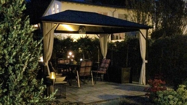 Een terras buiten met een overdekte zithoek, een tafel en stoelen.