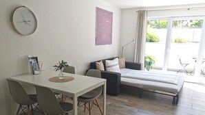A modern living room with a dining table, chairs, a sofa, and a bed.