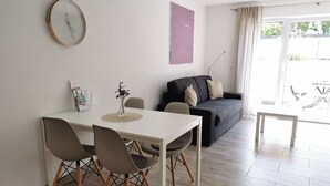 A modern living room with a dining table, chairs, a sofa, and a large window.
