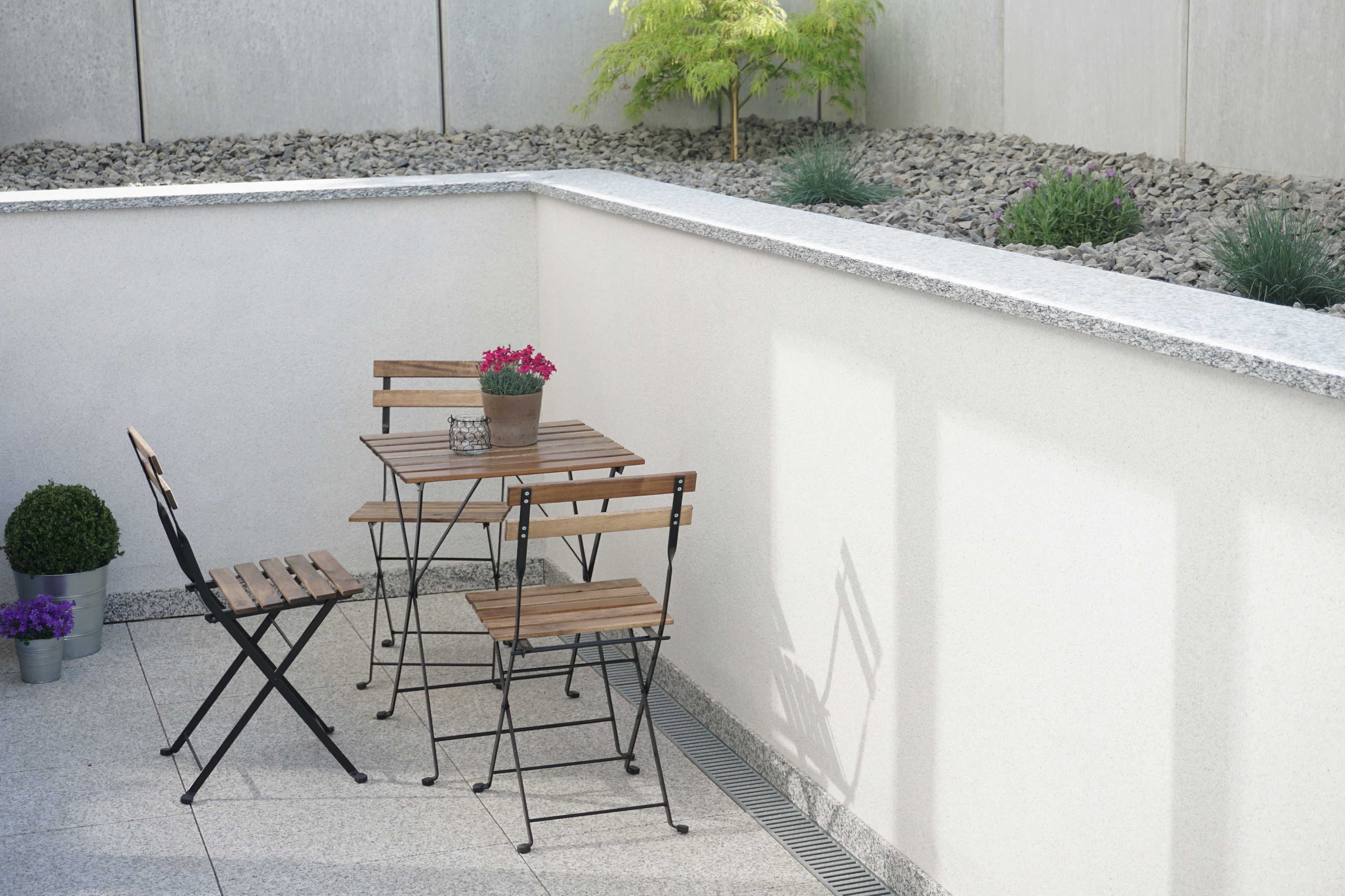 A small outdoor patio with a table and chairs, a potted plant, and a small tree.