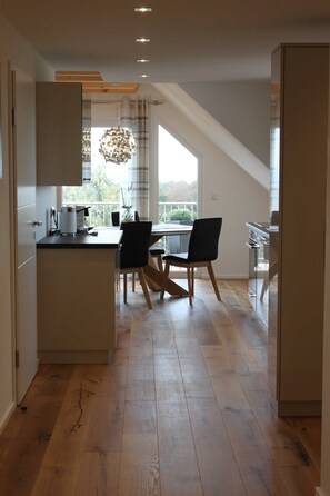 A modern kitchen with a dining area, wooden flooring, and a large window.