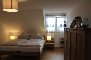 A bedroom with a bed, bedside lamps, a nightstand, a wooden wardrobe, and a window with curtains.