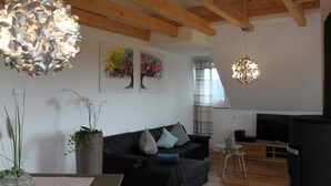 A modern living room with a black sofa, wooden beams, a TV, and abstract wall art. - flammende.aussicht, Germany (Freiamt)