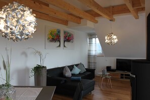 A modern living room with a black sofa, wooden beams, a TV, and abstract wall art.